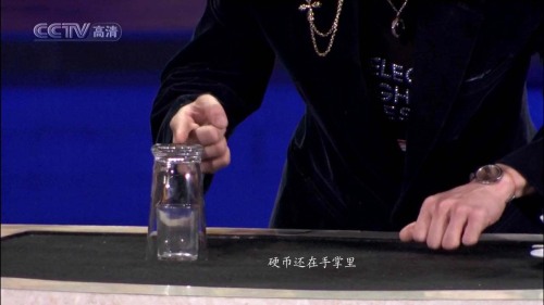 看似很嫻熟地把小玻璃杯放到桌面上,其實(shí)是非常仔細(xì)地放到出口的旁邊,這個(gè)位置要使硬幣出口處于小玻璃杯底座和大玻璃杯口之間.劉謙可以用右手或者腳啟動(dòng)一個(gè)隱蔽的開關(guān),使彈簧機(jī)構(gòu)動(dòng)作將硬幣彈射上去,這個(gè)機(jī)關(guān)我們不去思考了,因?yàn)楦静挥觅M(fèi)腦筋,這不是魔術(shù)的關(guān)鍵.硬幣彈射上去后,經(jīng)過小玻璃杯的杯口和大玻璃杯的內(nèi)杯壁之間的縫隙,上升到大玻璃杯的底座后,被反射回來,掉到小玻璃杯里.由于彈簧的發(fā)射速度快,硬幣上升過程用肉眼根本看不出來,人們只是看到硬幣瞬間在小玻璃杯里面,感到很驚奇.
